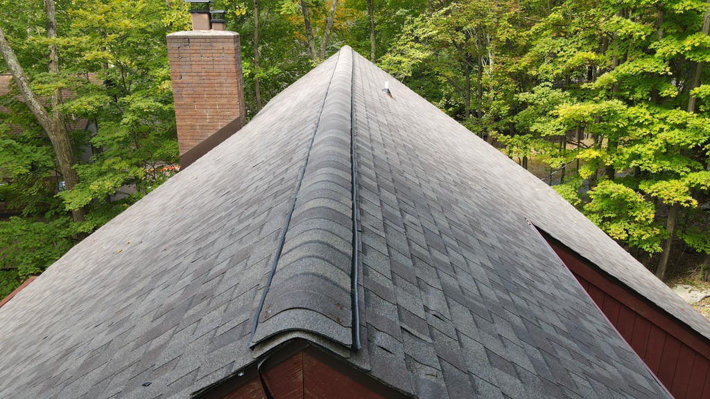 Close-up of a freshly installed shingle roof ridge line with a brick chimney